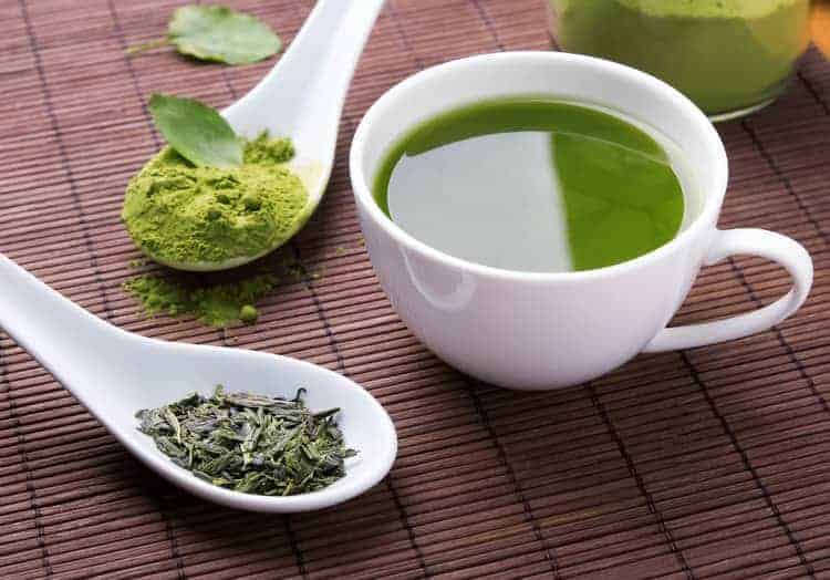 benefits of matcha and green tea for skincare: wooden spoon with matcha powder, tea in a cup and tea leaves on a mat